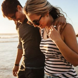 Guy walking on the beach with his arm around a girl after telling her he likes her